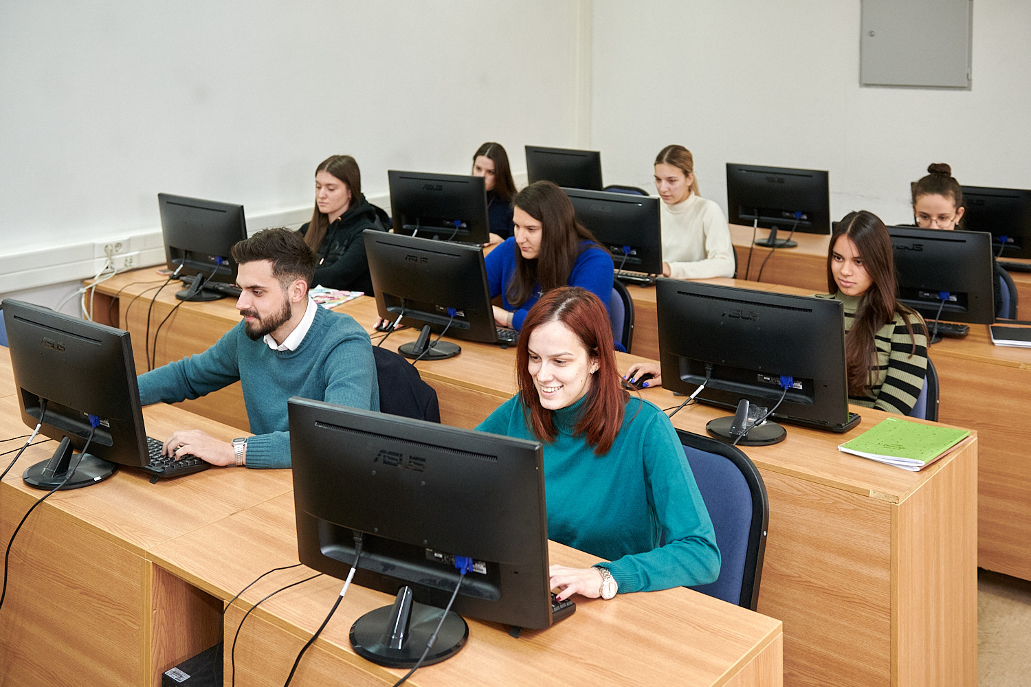 Estudantes, maioritariamente mulheres, trabalham em computadores numa sala de informática.