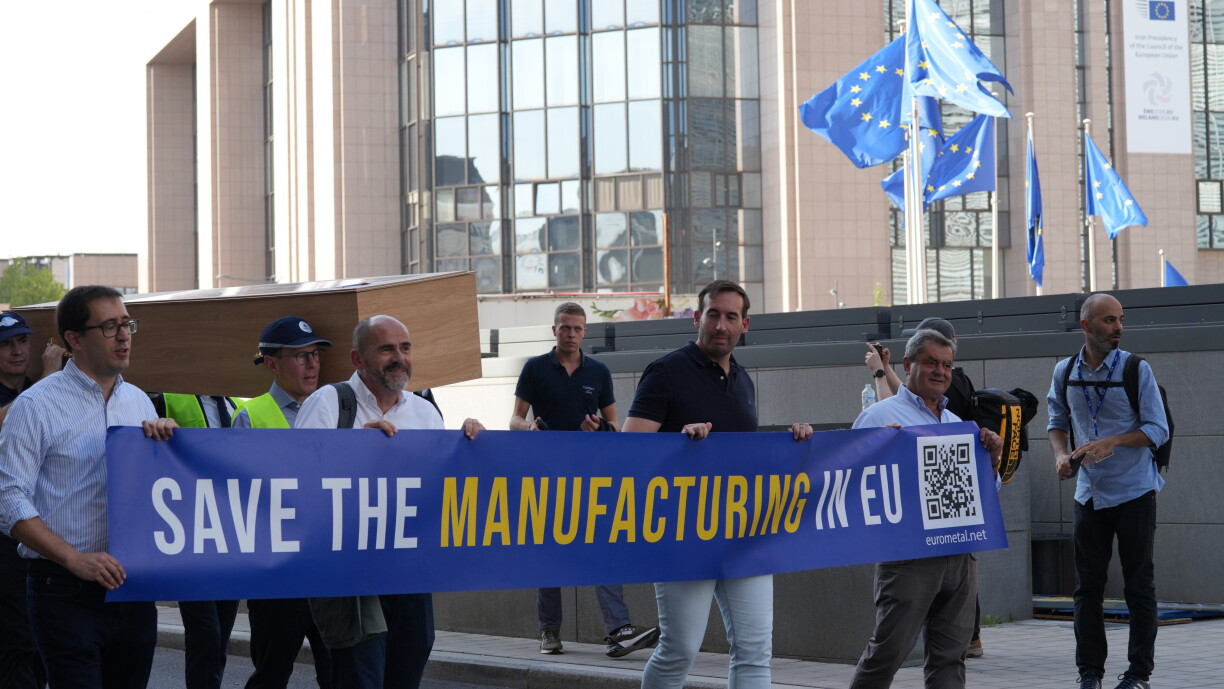 Participantes seguram uma faixa Save the Manufacturing in EU em frente a um edifício europeu.